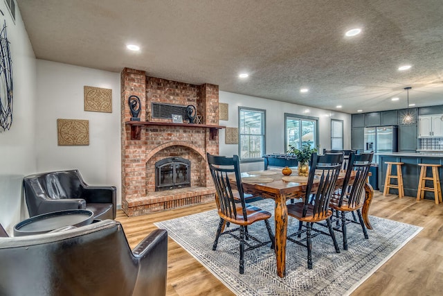 dining room with a brick fireplace, a textured ceiling, and light hardwood / wood-style floors