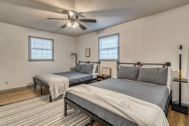 bedroom featuring ceiling fan, a textured ceiling, light hardwood / wood-style floors, and multiple windows