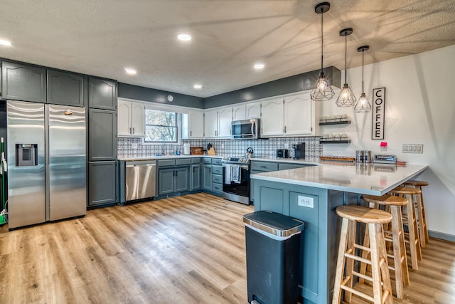 kitchen with appliances with stainless steel finishes, kitchen peninsula, decorative light fixtures, and light wood-type flooring