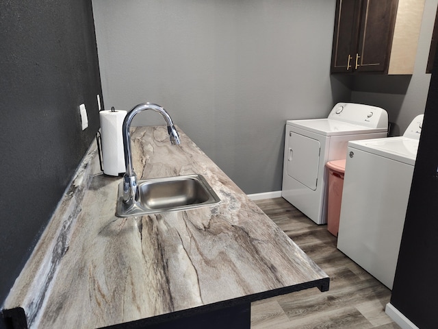 clothes washing area featuring washing machine and dryer, sink, wood-type flooring, and cabinets