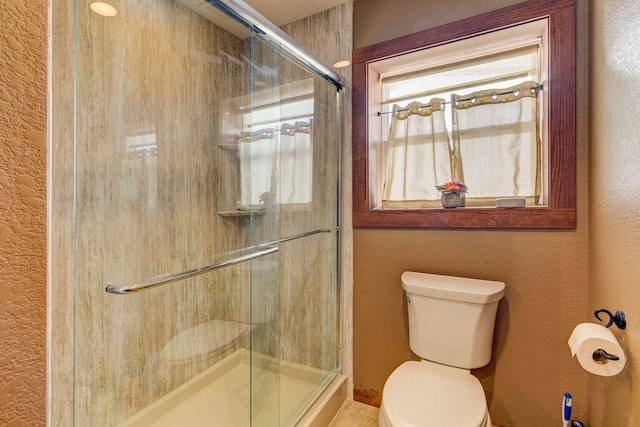 bathroom featuring a shower with door and toilet