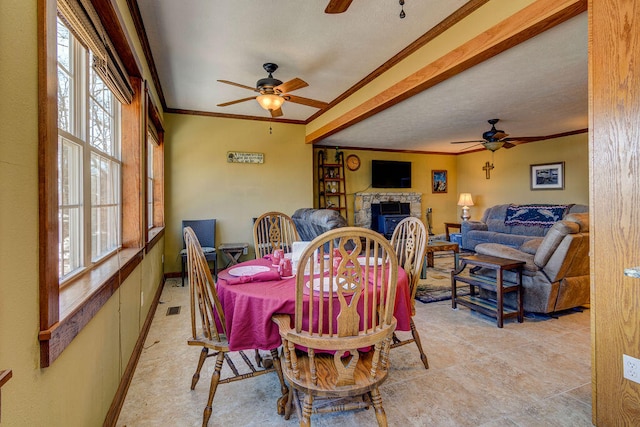 dining room featuring ceiling fan, ornamental molding, and a stone fireplace