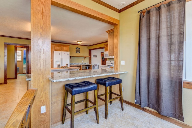 kitchen with light stone countertops, white appliances, kitchen peninsula, a breakfast bar area, and ornamental molding