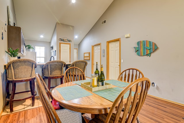 dining room with light wood-type flooring and high vaulted ceiling