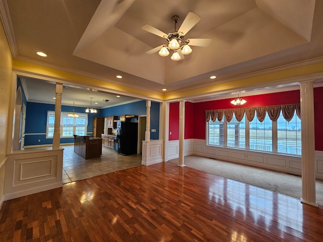 unfurnished living room featuring ornamental molding, ceiling fan with notable chandelier, carpet, and a raised ceiling