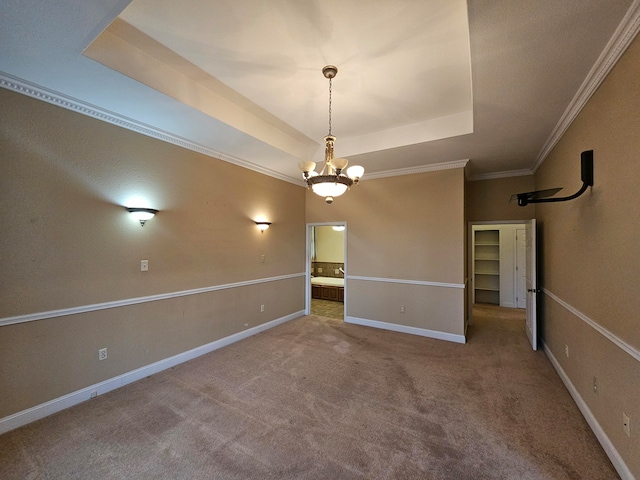 carpeted spare room with an inviting chandelier, a tray ceiling, and crown molding