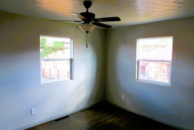 empty room with dark hardwood / wood-style flooring, a wealth of natural light, and ceiling fan