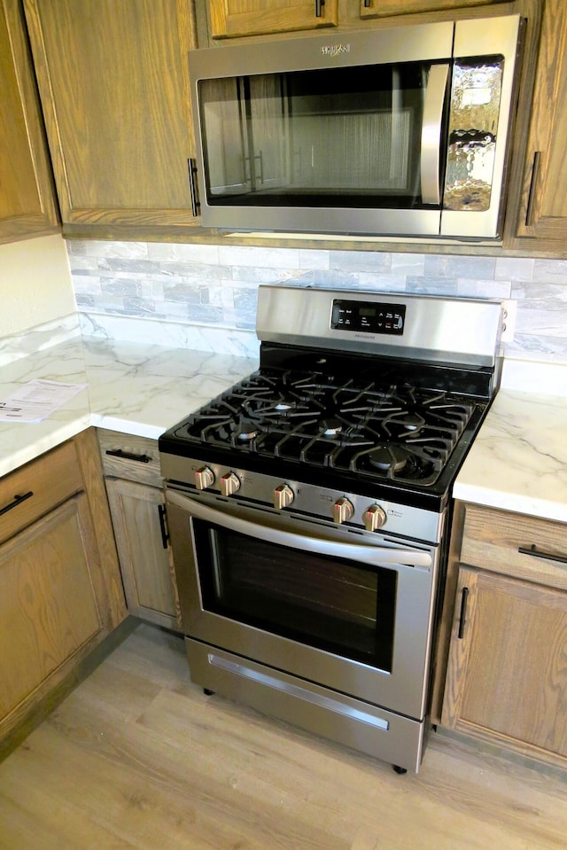 kitchen with stainless steel appliances, light stone countertops, backsplash, and light hardwood / wood-style flooring