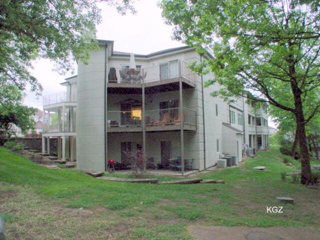 rear view of house with a balcony, a yard, and central air condition unit