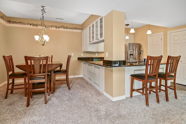 kitchen with kitchen peninsula, white cabinets, decorative light fixtures, and light colored carpet