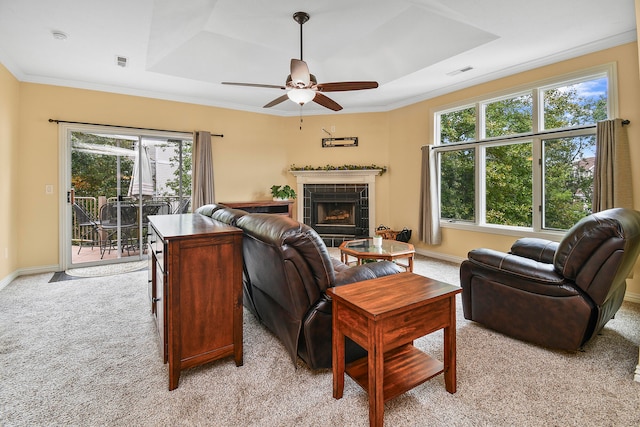 carpeted living room with ornamental molding, a tray ceiling, a tile fireplace, and a healthy amount of sunlight