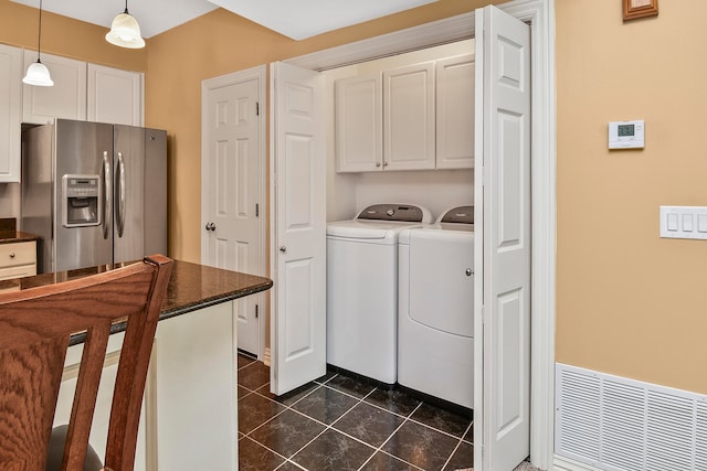 laundry area featuring washing machine and clothes dryer, dark tile patterned flooring, and cabinets