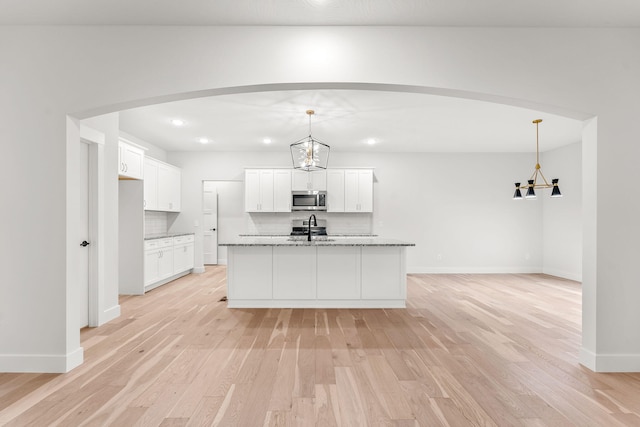 kitchen featuring hanging light fixtures, light hardwood / wood-style flooring, light stone counters, and white cabinetry