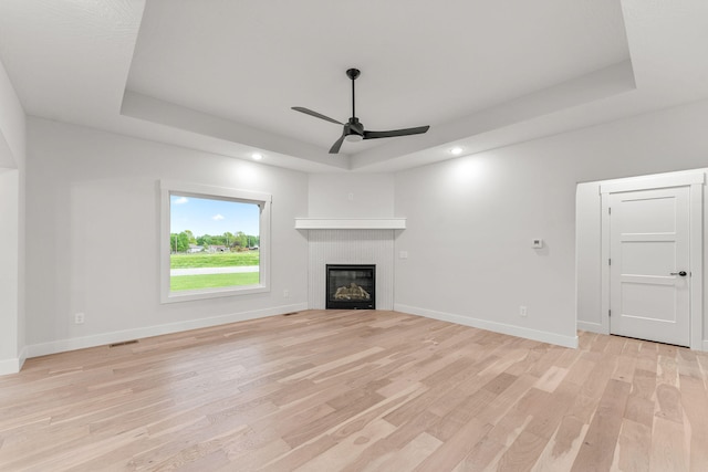 unfurnished living room with ceiling fan, light hardwood / wood-style floors, and a raised ceiling