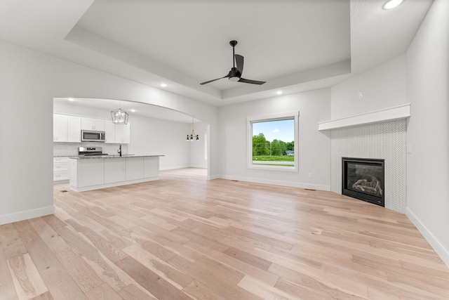 unfurnished living room featuring ceiling fan, light hardwood / wood-style flooring, a fireplace, and a raised ceiling