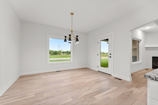 unfurnished dining area with a fireplace, light hardwood / wood-style floors, and an inviting chandelier