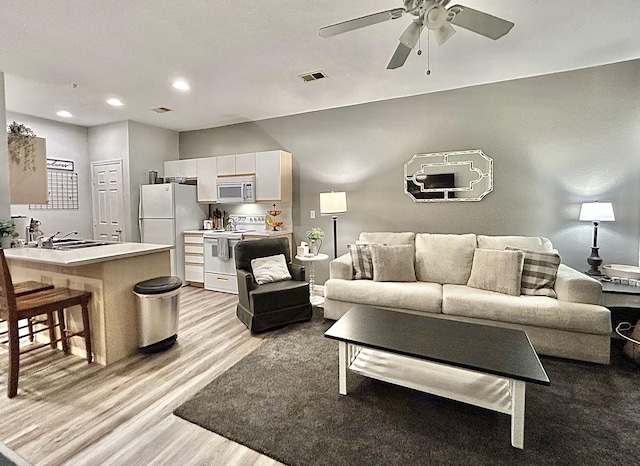 living room with light wood-type flooring, ceiling fan, and sink