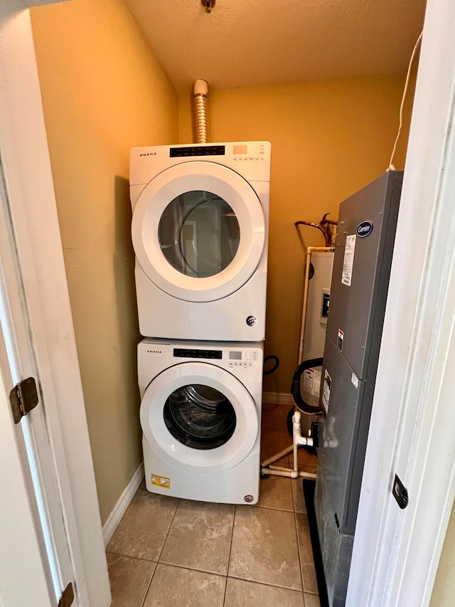 clothes washing area with stacked washer / drying machine, light tile patterned floors, and a textured ceiling