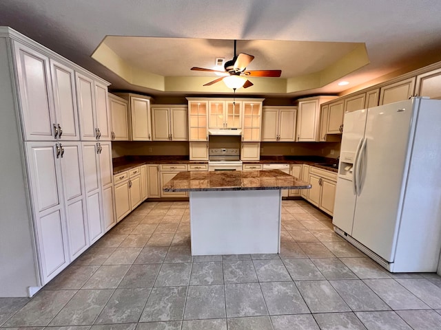 kitchen with a center island, white fridge with ice dispenser, a tray ceiling, and stainless steel stove