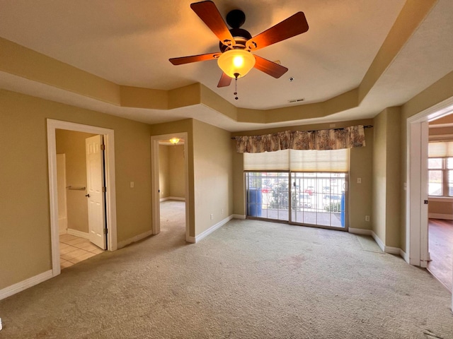 empty room featuring a raised ceiling, light colored carpet, and ceiling fan