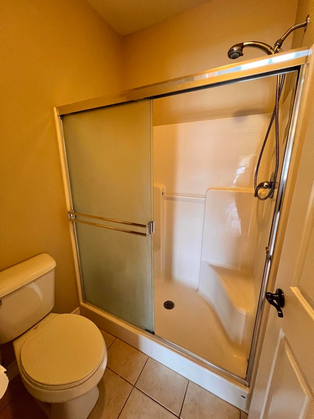 bathroom with tile patterned flooring, a shower with shower door, and toilet