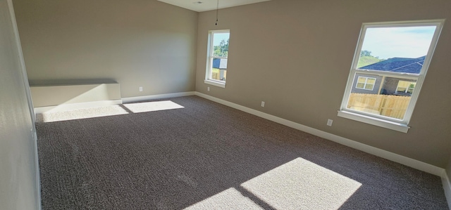 spare room with dark colored carpet and a healthy amount of sunlight