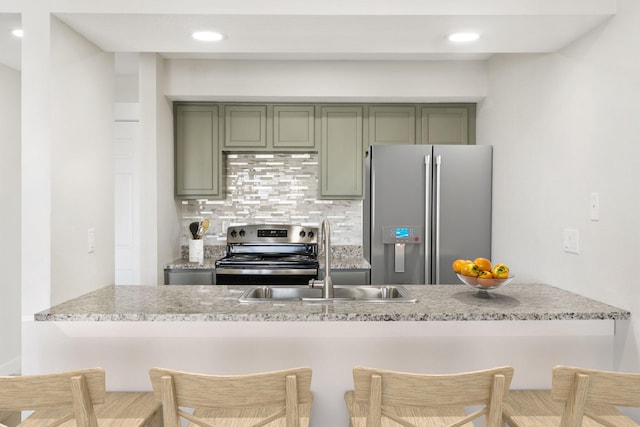 kitchen with sink, tasteful backsplash, green cabinetry, appliances with stainless steel finishes, and a kitchen breakfast bar