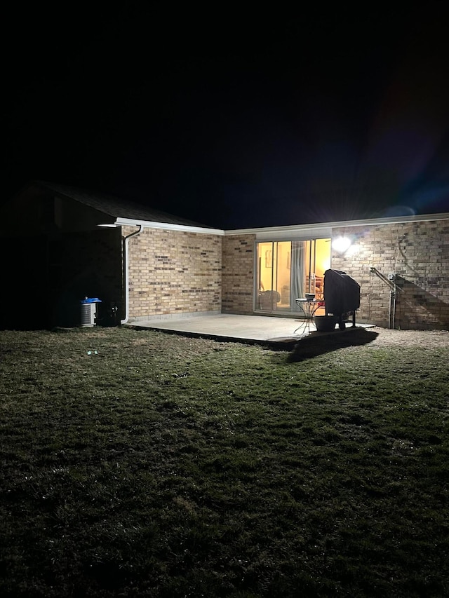 back house at twilight featuring a patio and a lawn