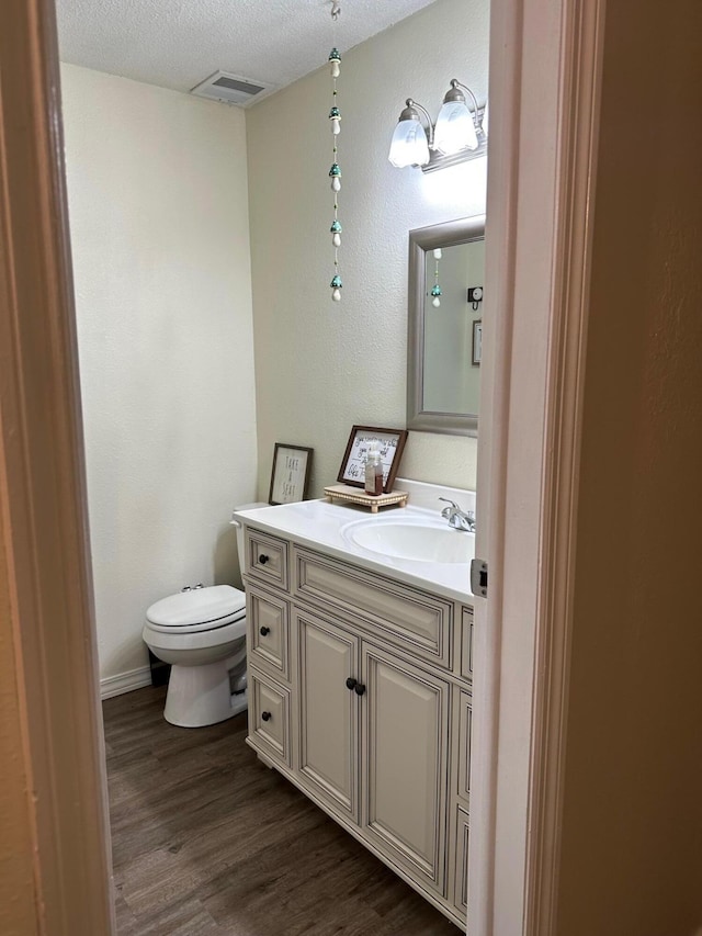 bathroom with a textured ceiling, wood-type flooring, vanity, and toilet