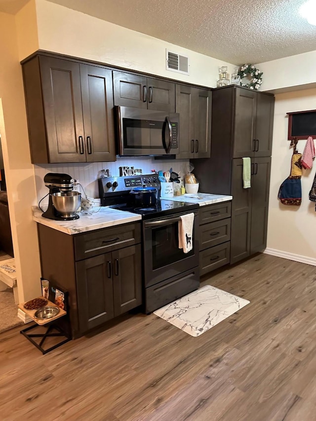 kitchen featuring wood-type flooring, appliances with stainless steel finishes, dark brown cabinetry, and a textured ceiling