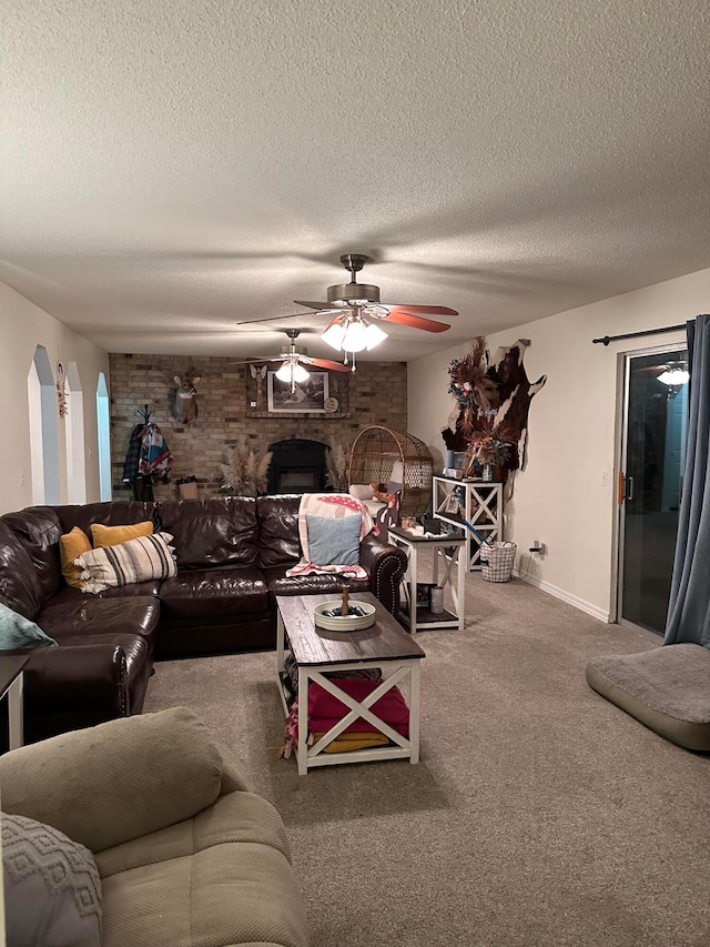 carpeted living room featuring a brick fireplace, ceiling fan, brick wall, and a textured ceiling