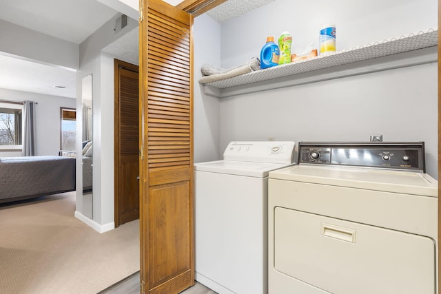 clothes washing area with light carpet, a textured ceiling, and washer and dryer