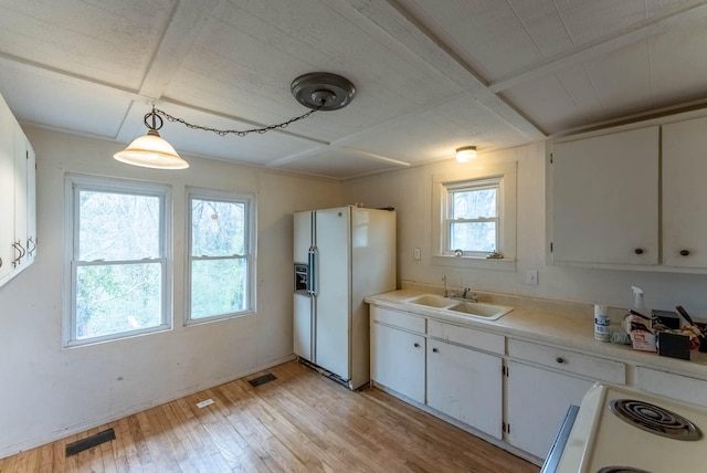 kitchen featuring white fridge with ice dispenser, decorative light fixtures, plenty of natural light, and white cabinetry