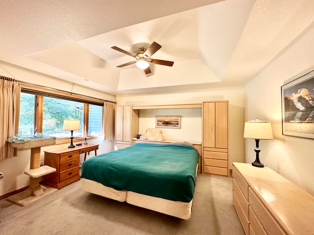 bedroom featuring a textured ceiling, light carpet, ceiling fan, and a raised ceiling