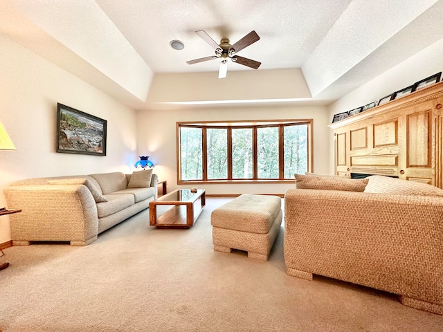 living room with ceiling fan, a tray ceiling, carpet flooring, and a textured ceiling