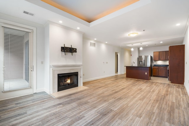 unfurnished living room with sink, light wood-type flooring, and ornamental molding