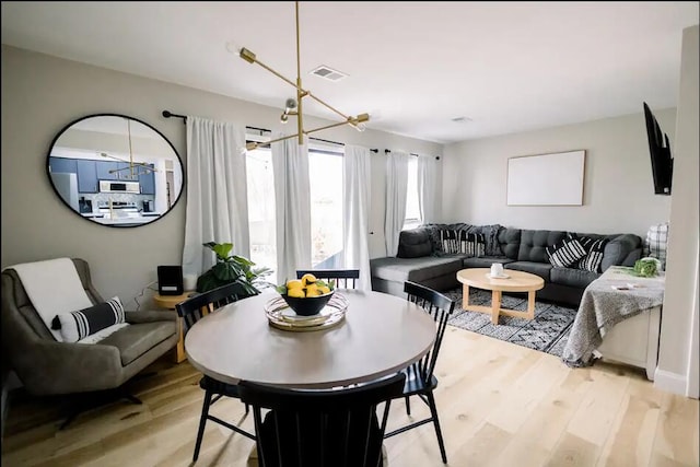 dining area featuring visible vents, light wood finished floors, and an inviting chandelier