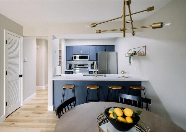 kitchen with stainless steel appliances, a breakfast bar, a sink, light wood-type flooring, and a peninsula