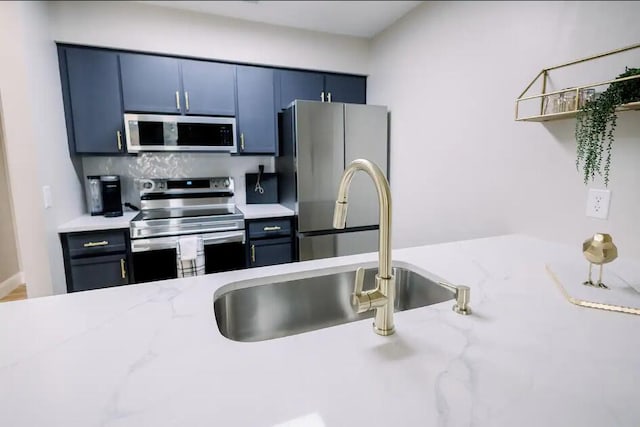 kitchen featuring blue cabinetry, open shelves, a sink, light stone countertops, and appliances with stainless steel finishes