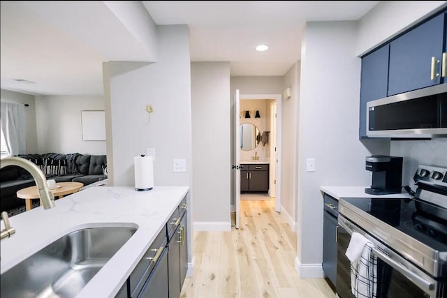 kitchen with stainless steel appliances, a sink, recessed lighting, light wood-style floors, and blue cabinetry
