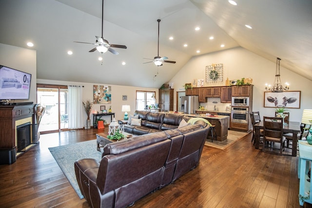 living room featuring ceiling fan with notable chandelier, dark wood-type flooring, and high vaulted ceiling