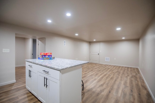 kitchen with white cabinets, light stone countertops, light hardwood / wood-style floors, and a center island