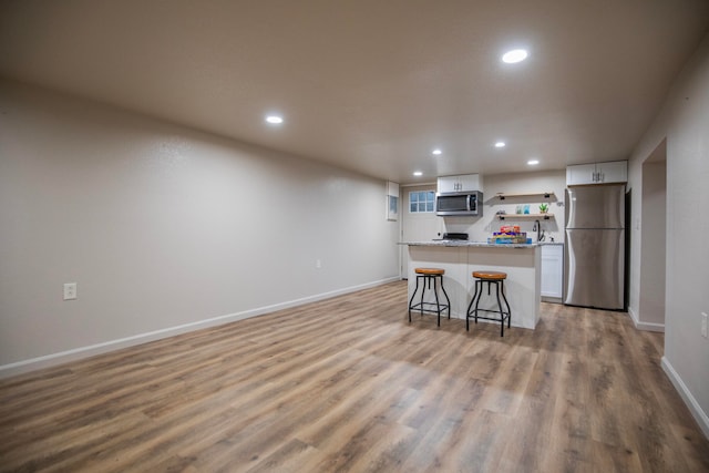 kitchen featuring light hardwood / wood-style floors, a kitchen breakfast bar, white cabinets, appliances with stainless steel finishes, and a center island