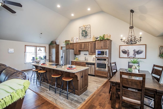 kitchen with light wood-type flooring, stainless steel appliances, pendant lighting, vaulted ceiling, and a kitchen breakfast bar