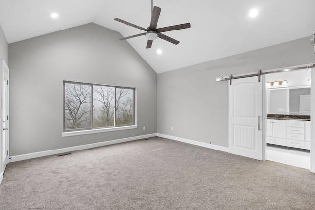 interior space with a barn door, light carpet, connected bathroom, and high vaulted ceiling