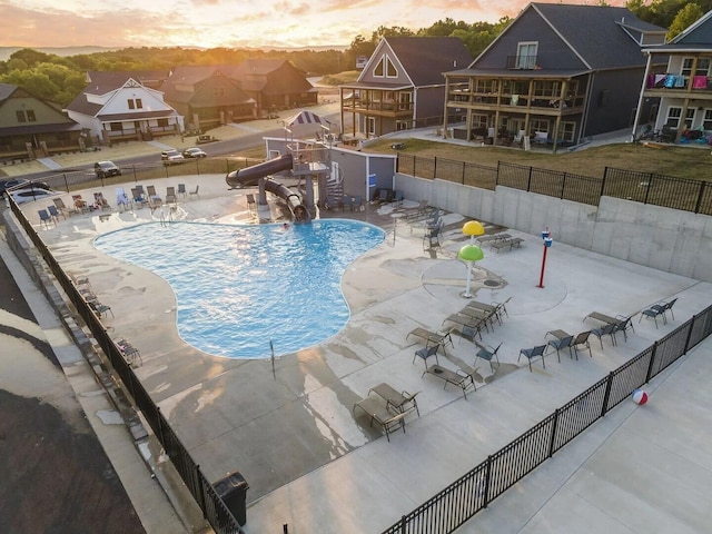 pool at dusk featuring a water slide and a patio area