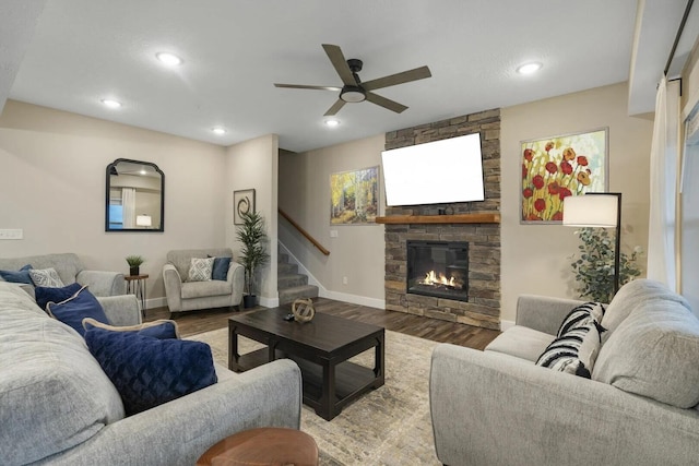 living room with wood-type flooring, ceiling fan, and a stone fireplace