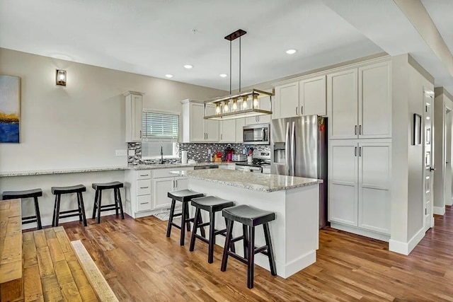 kitchen featuring wood-type flooring, a breakfast bar area, light stone countertops, hanging light fixtures, and appliances with stainless steel finishes