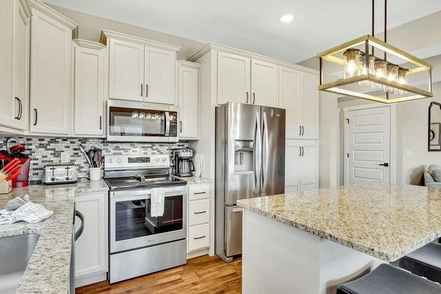 kitchen featuring light wood-type flooring, hanging light fixtures, appliances with stainless steel finishes, a breakfast bar area, and light stone countertops