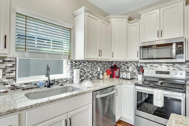 kitchen featuring tasteful backsplash, light stone countertops, appliances with stainless steel finishes, and sink